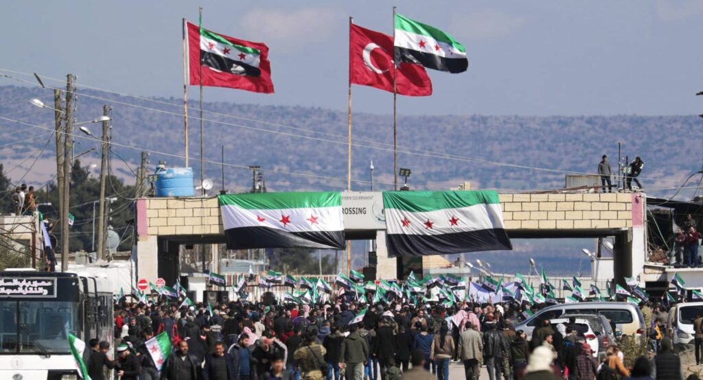Displaced Syrians hold Syrian opposition flags during a rally in support of the Turkish army and Syrian rebels at the Bab el-Salam border crossing, February 2020. Photo credit: REUTERS/Khalil Ashawi.